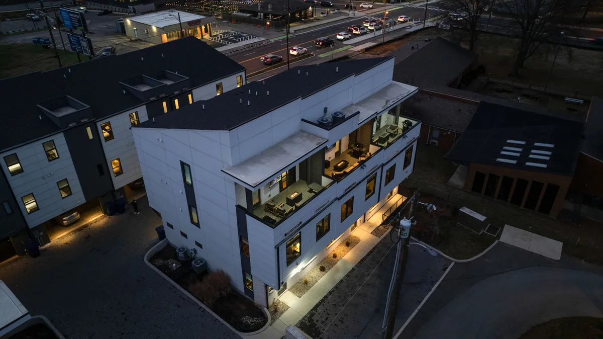 An exterior shot featuring modern architecture with illuminated windows and an inviting outdoor seating area. The scene evokes stylish, hotel-level luxury and readiness for evening entertaining, suggesting the blend of private comfort and public vibrancy described in the section.