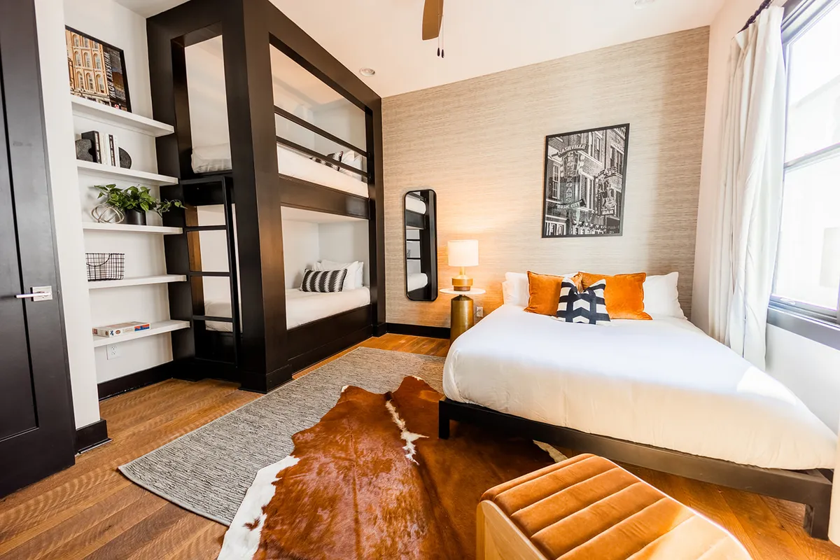 A welcoming bedroom setup with bunk beds and a separate bed accented in orange. Stylish artwork on the wall and a cozy rug ground the space, making it ideal for families or groups seeking flexible sleeping arrangements.