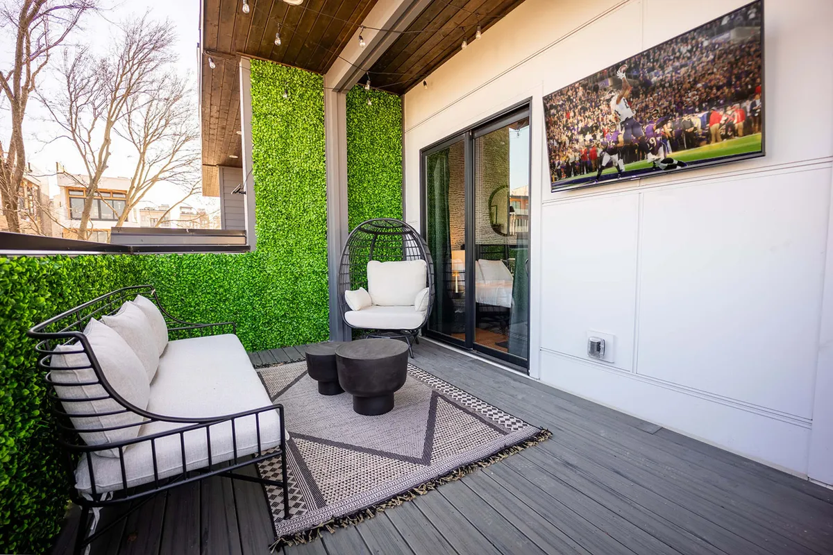 An inviting rooftop deck with a lush green wall, a stylish hanging chair, a cozy coffee table, and a prominent flat screen TV—perfect for watching sports. The space is illuminated with warm lighting, and an outdoor grill area is visible, making it ideal for social gatherings and barbecues.