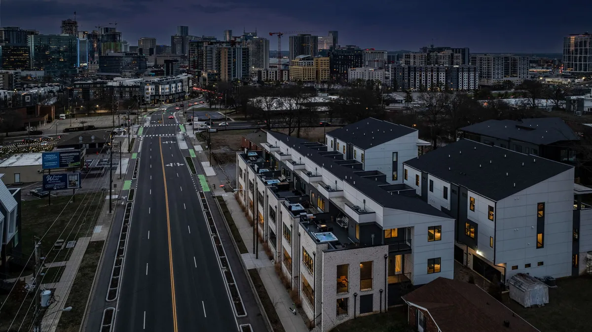 This exterior image captures modern townhouses illuminated against the backdrop of the city skyline at dusk. Rooftop areas and windows glow with warm light, hinting at lively gatherings above. The city’s vibrant energy is felt through the interplay of streetlights and skyline views, evoking the sensation of celebrating on a rooftop while the city comes alive below.