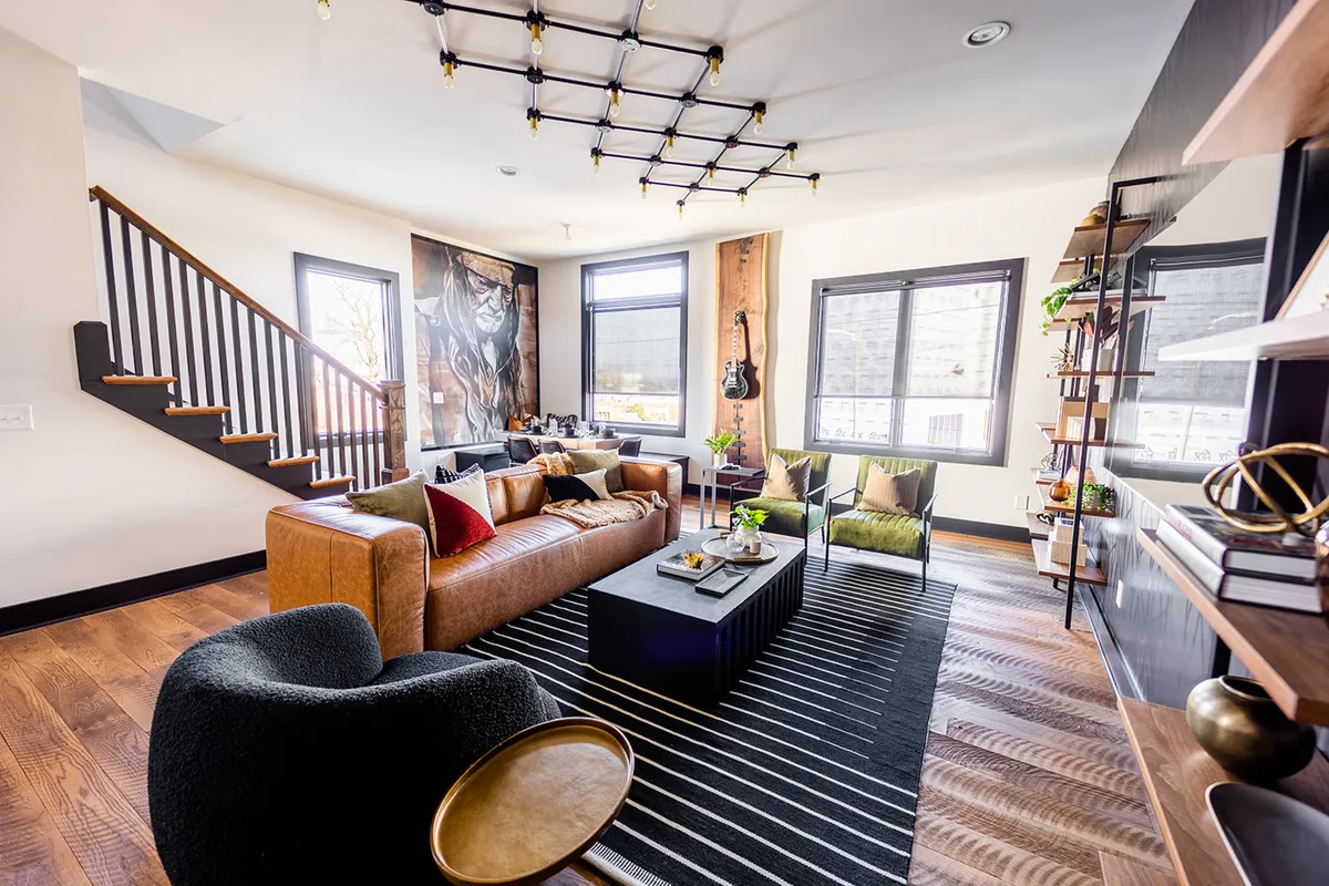 A designer living room with a leather sofa, black coffee table, striking wall artwork, a guitar hanging as decor, and stylish chairs. The setting is both contemporary and comfortable, with creative accents that evoke Nashville’s music culture.