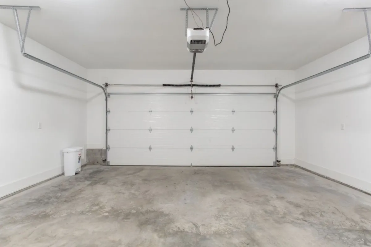 A functional garage space with a large garage door, ceiling lights, and a concrete floor. The neutral setting is ideal for storing roll-away beds and other additional sleeping options, highlighting practical amenities for larger groups.